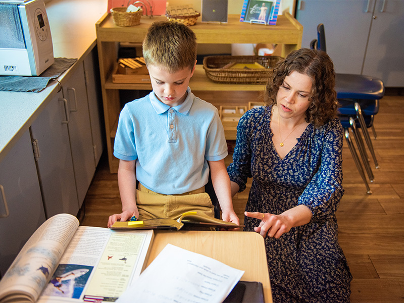 Teacher working with a student who is reading a book.