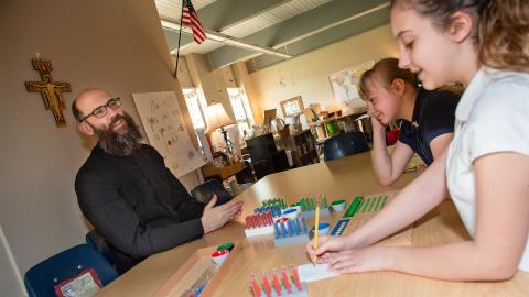 Two students learning math from a teaching priest.